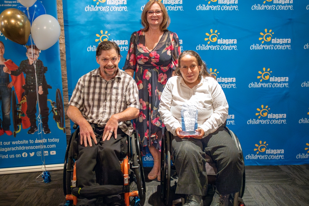 Man and women in wheelchairs with women standing behind in front of blue backdrop